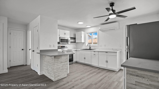 2430 W Ave, Rifle, CO 81650 - kitchen with appliances with stainless steel finishes, an AC wall unit, a peninsula, white cabinets, and light wood finished floors