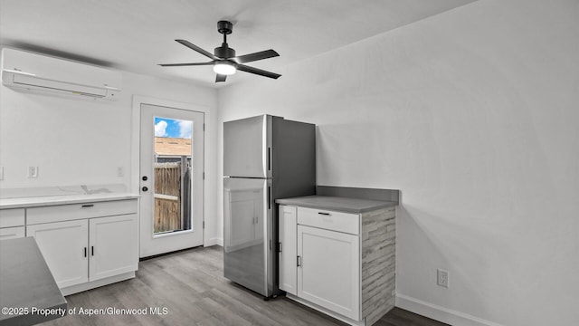 2430 W Ave, Rifle, CO 81650 - kitchen featuring a wall unit AC, freestanding refrigerator, white cabinetry, wood finished floors, and a ceiling fan