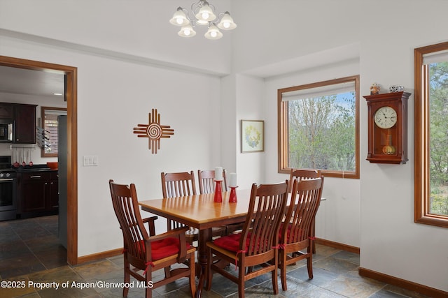 dining room with stone tile floors, baseboards, a notable chandelier, and a wealth of natural light