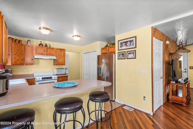 kitchen with a breakfast bar, white appliances, sink, dark hardwood / wood-style floors, and kitchen peninsula