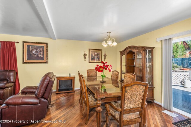 dining area featuring beamed ceiling, wood-type flooring, and an inviting chandelier