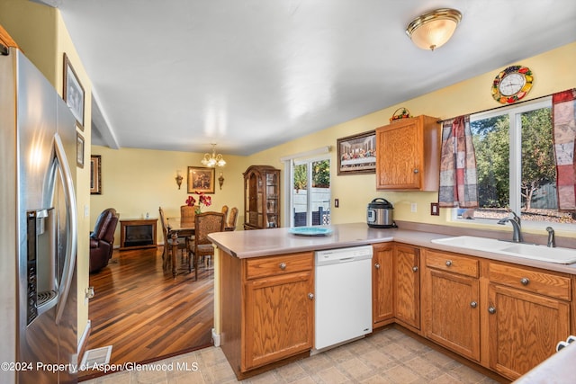 kitchen with an inviting chandelier, white dishwasher, sink, stainless steel refrigerator with ice dispenser, and kitchen peninsula