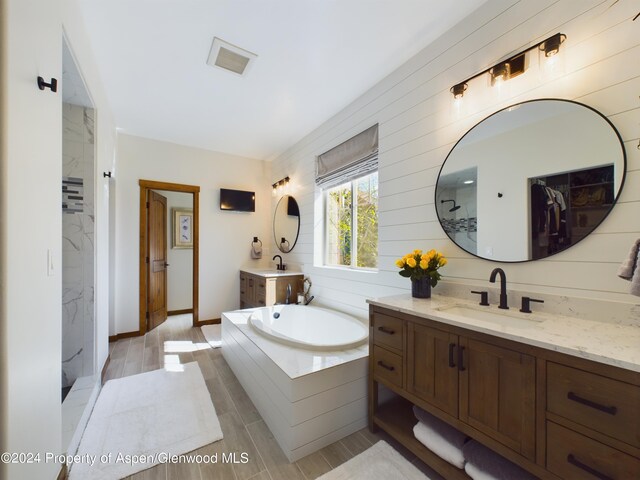 bathroom with a marble finish shower, wood finish floors, two vanities, a sink, and a garden tub