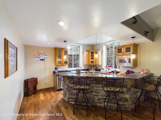 kitchen with stainless steel microwave, a kitchen breakfast bar, a peninsula, and dark wood finished floors