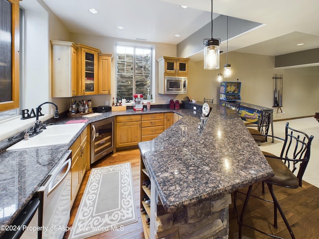 kitchen with wine cooler, pendant lighting, light wood-style flooring, appliances with stainless steel finishes, and a sink