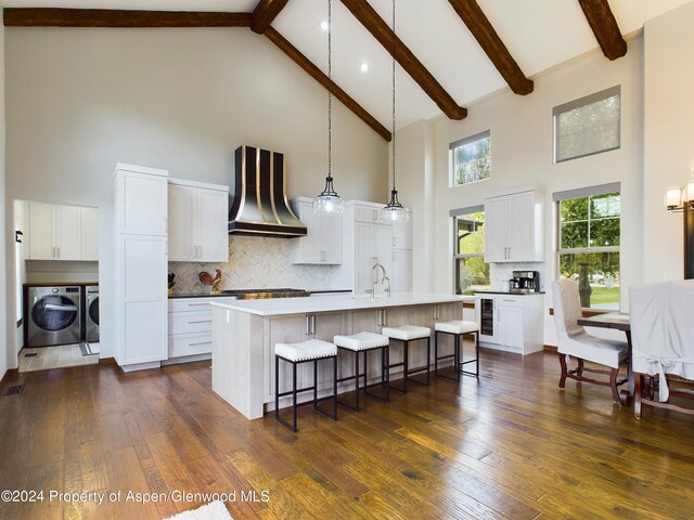 kitchen with washer and dryer, a kitchen breakfast bar, dark wood finished floors, wine cooler, and wall chimney exhaust hood