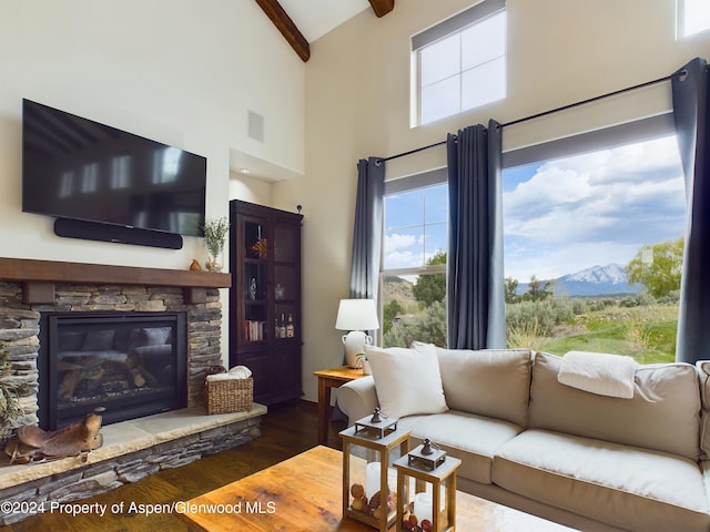 living area featuring beamed ceiling, high vaulted ceiling, wood finished floors, a mountain view, and a stone fireplace