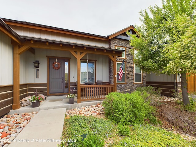 property entrance featuring stone siding, covered porch, and board and batten siding