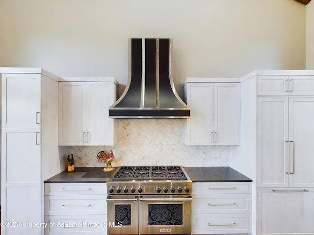 kitchen with range with two ovens, white cabinets, dark countertops, wall chimney range hood, and backsplash