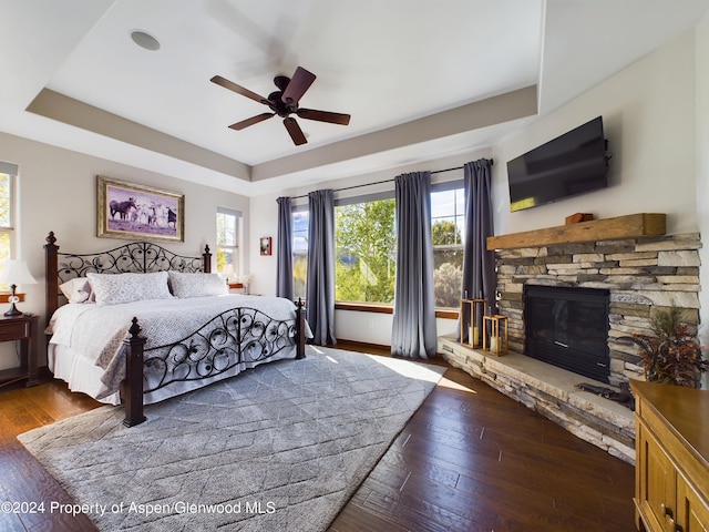 bedroom featuring a ceiling fan, wood-type flooring, a raised ceiling, and a fireplace