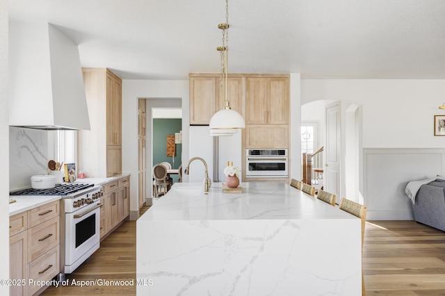 kitchen featuring light brown cabinets, white appliances, wall chimney range hood, sink, and tasteful backsplash