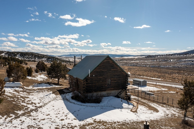 view of snowy exterior featuring fence, a mountain view, metal roof, and log exterior