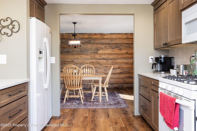 kitchen with pendant lighting, dark wood finished floors, log walls, light countertops, and white appliances