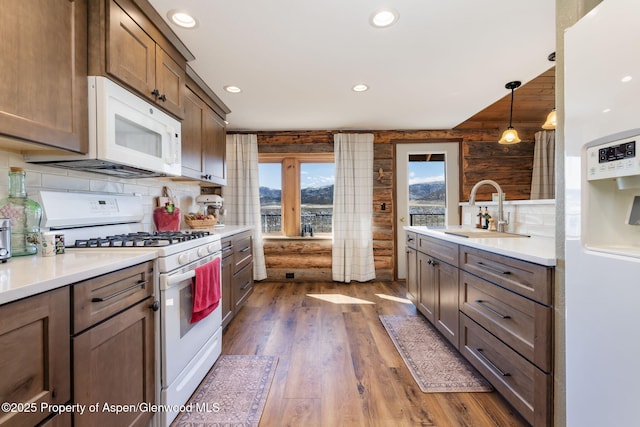 kitchen featuring white appliances, dark wood finished floors, decorative light fixtures, light countertops, and a sink