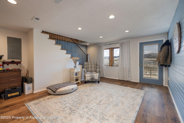 living area with dark wood-type flooring, electric panel, visible vents, and stairs