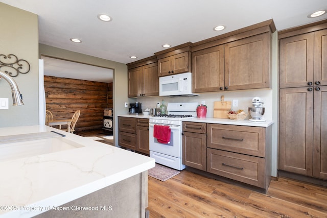 kitchen featuring light wood-type flooring, white appliances, rustic walls, and recessed lighting