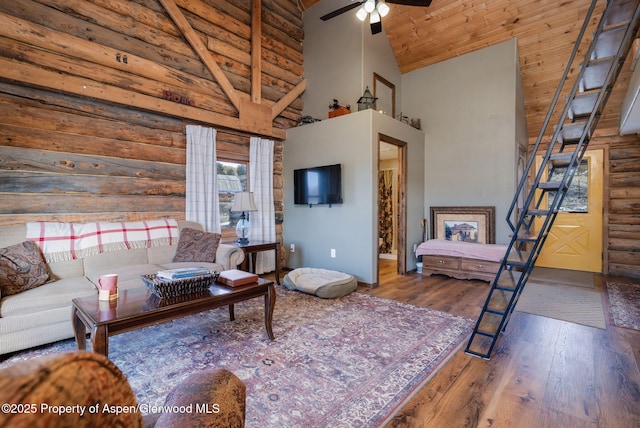 living area with high vaulted ceiling, wooden ceiling, wood finished floors, stairway, and rustic walls