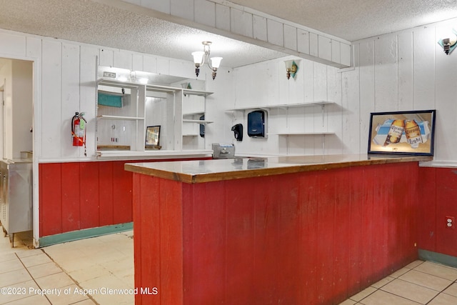 kitchen featuring wood walls, kitchen peninsula, a textured ceiling, and light tile patterned floors