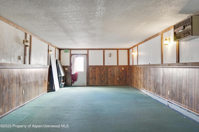 spare room with baseboard heating, wood walls, light colored carpet, and a textured ceiling