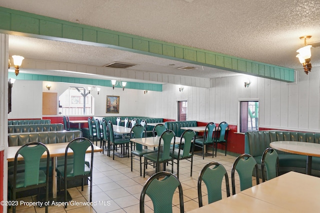 dining area with light tile patterned flooring, a textured ceiling, and wooden walls