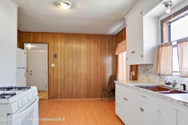 kitchen featuring white appliances, sink, white cabinets, light hardwood / wood-style floors, and wood walls