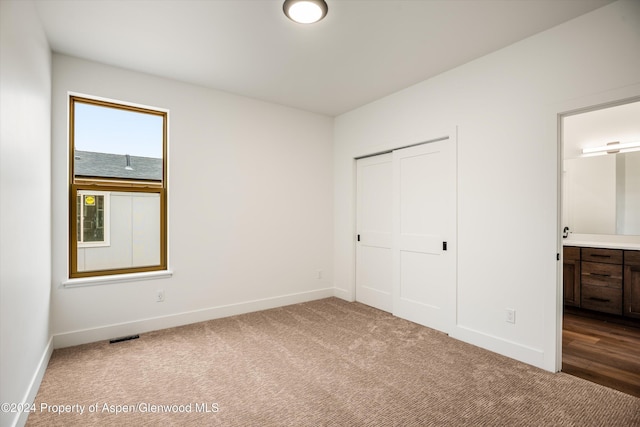 unfurnished bedroom featuring ensuite bath, a closet, and carpet flooring