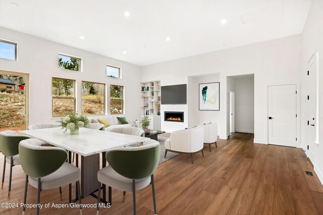 dining space with a lit fireplace, visible vents, wood finished floors, and recessed lighting