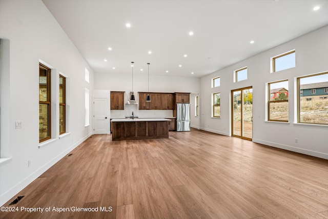 kitchen with stainless steel refrigerator, hanging light fixtures, a high ceiling, a center island, and light hardwood / wood-style floors