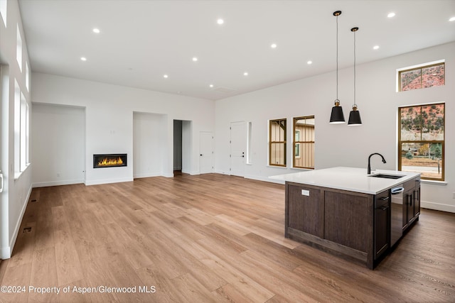 kitchen with an island with sink, sink, hanging light fixtures, dark brown cabinetry, and light wood-type flooring