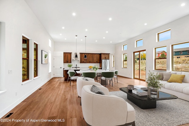 living area featuring a high ceiling, light wood-style flooring, baseboards, and recessed lighting