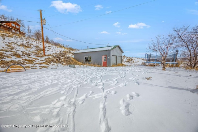 snowy yard with a trampoline, an outdoor structure, and a garage