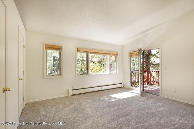 carpeted empty room with vaulted ceiling and a baseboard heating unit