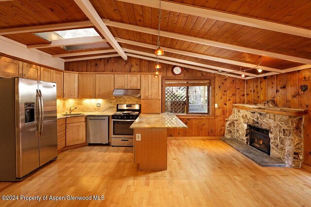 kitchen with appliances with stainless steel finishes, lofted ceiling with beams, a fireplace, light hardwood / wood-style floors, and a kitchen island