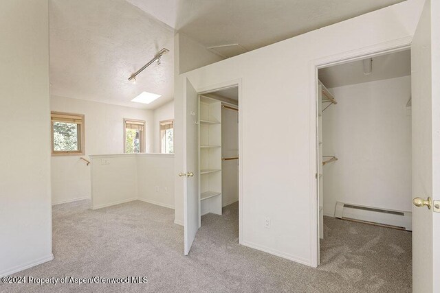 interior space featuring vaulted ceiling, light colored carpet, and a baseboard heating unit