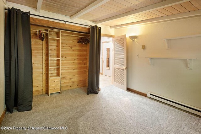 interior space with wood walls, baseboard heating, beam ceiling, carpet floors, and a closet