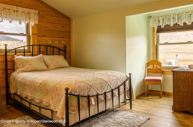 bedroom with wood-type flooring, wooden walls, and vaulted ceiling