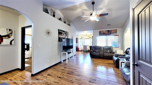 living room with hardwood / wood-style floors, ceiling fan with notable chandelier, and vaulted ceiling