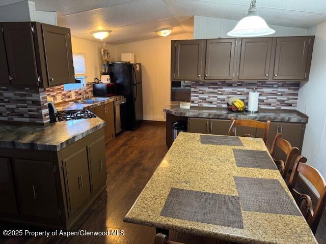kitchen with dark wood-style floors, backsplash, freestanding refrigerator, a kitchen bar, and hanging light fixtures