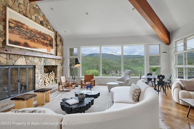 living room featuring light wood-type flooring, vaulted ceiling with beams, and a stone fireplace