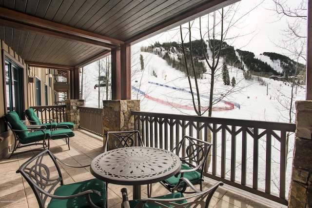 snow covered back of property with a mountain view and covered porch