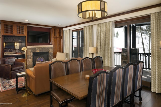 dining room with ornamental molding, a stone fireplace, and dark wood-type flooring