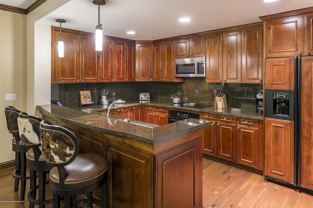 kitchen with kitchen peninsula, a kitchen breakfast bar, sink, black appliances, and hanging light fixtures