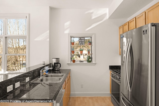 kitchen featuring stainless steel appliances, sink, kitchen peninsula, light hardwood / wood-style flooring, and dark stone counters