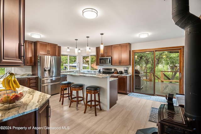 kitchen with light stone countertops, stainless steel appliances, pendant lighting, light hardwood / wood-style flooring, and a center island