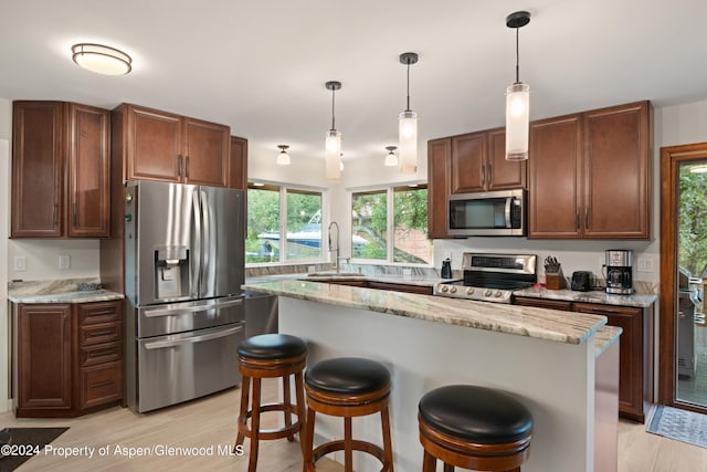 kitchen featuring appliances with stainless steel finishes, light wood-type flooring, light stone counters, decorative light fixtures, and a kitchen island