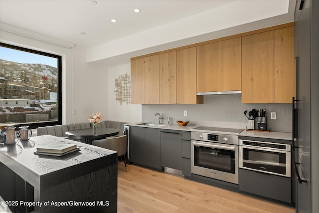 kitchen featuring sink, backsplash, light hardwood / wood-style flooring, and stainless steel oven