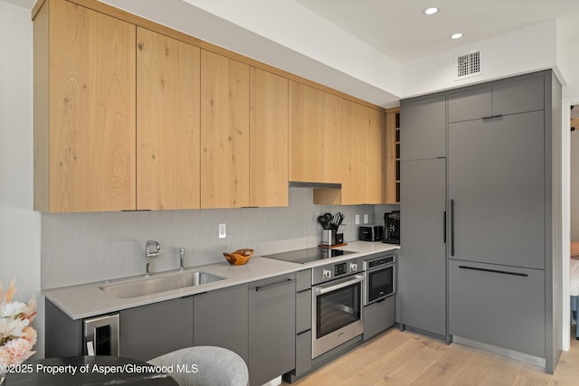 kitchen featuring black electric stovetop, tasteful backsplash, sink, light hardwood / wood-style flooring, and oven