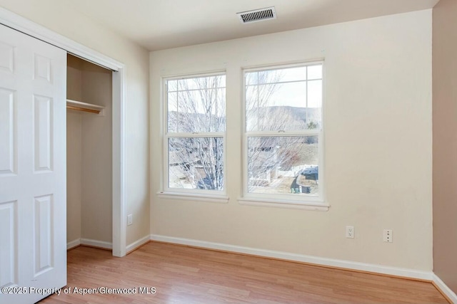 unfurnished bedroom with wood finished floors, visible vents, baseboards, and multiple windows