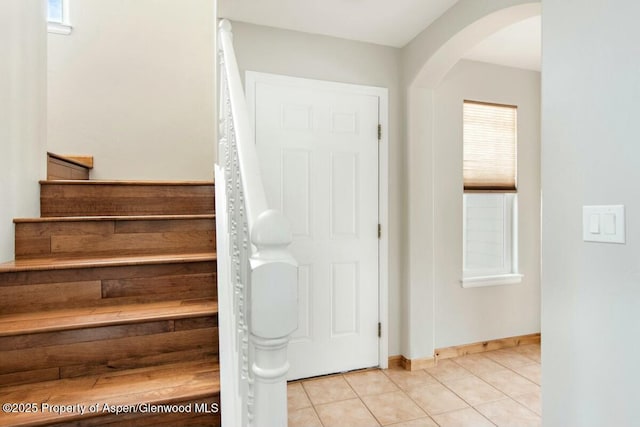 staircase with baseboards, arched walkways, and tile patterned floors