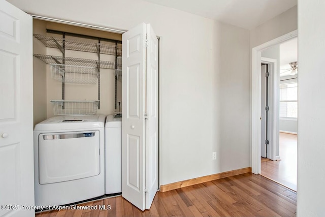 laundry area with laundry area, washer and clothes dryer, hardwood / wood-style flooring, and baseboards